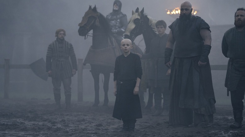 Dexter Sol Ansell als Egg staande in een modderig veld voor William Houston als Ser Robyn Rhysling en Youssef Kerkour als Steely Pate in A Knight of the Seven Kingdoms