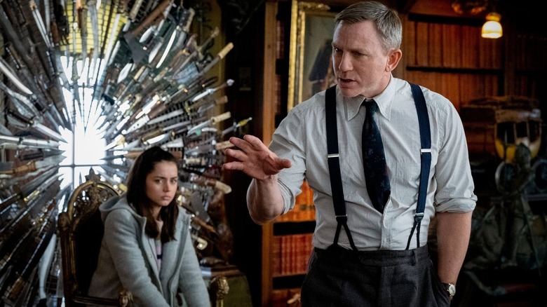 Ana de Armas as Marta Cabrera sitting in front of a display full of knives as Daniel Craig as Benoit Blanc stands in front of her in Knives Out