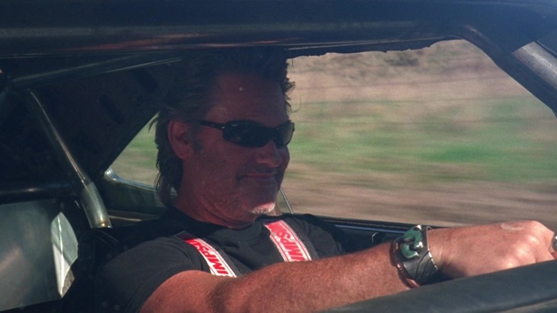 Kurt Russell as Stuntman Mike, wearing sunglasses, driving, and smiling in Death Proof