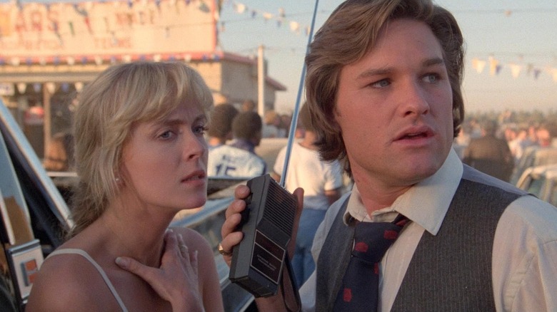 Deborah Harmon as Barbara Jane Fuchs standing next to Kurt Russell as Rudy Russo (who's holding a walkie-talkie) in Used Cars