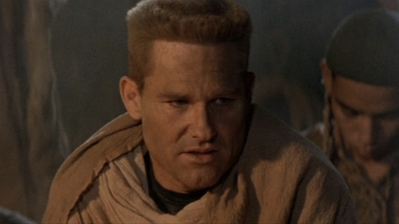 Kurt Russell's Jack O'Neill looks across frame as a man bows his head in the background in Stargate