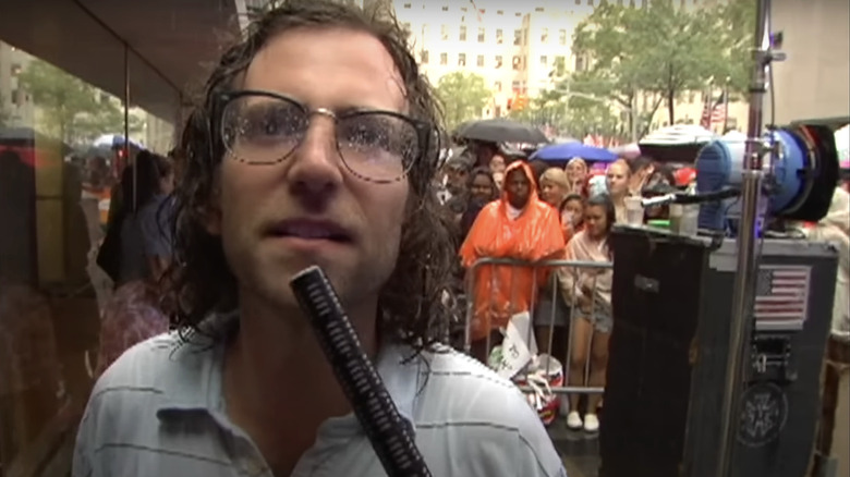 Kyle Mooney holds a microphone as he stands outside filming a report for Saturday Night LIve.