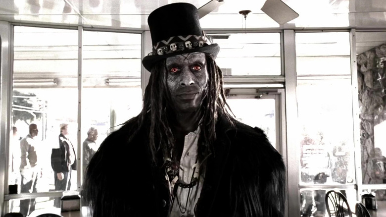 Papa Legba standing in restaurant in top hat and coat in American Horror Story