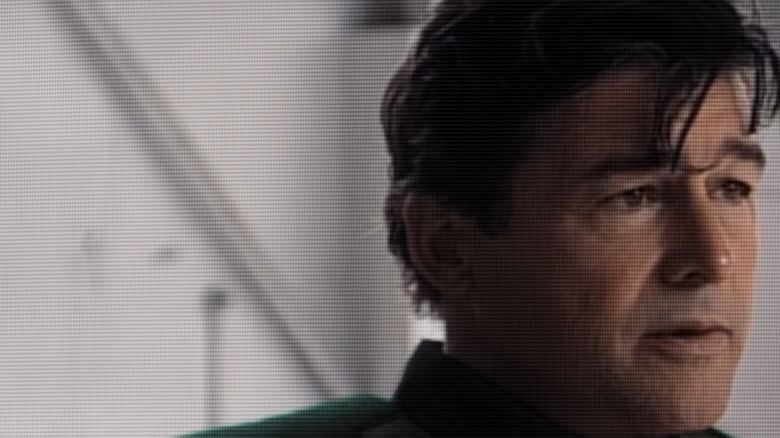 Kyle Chandler as Hal Stewart wearing a green superhero suit and doing an interview on TV in Lanterns