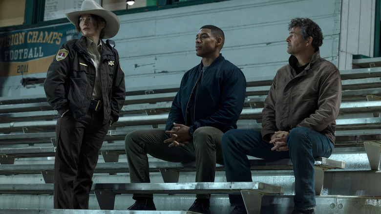 Kelly Macdonald as Sheriff Kerry Kane standing by a section of stadium bleachers next to Aaron Pierre as John Stewart and Kyle Chandler as Hal Jordan in Lanterns