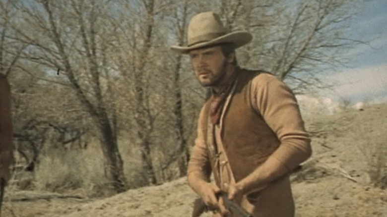 Lee Majors' Blue walks across the plains holding a rifle in Will Penny