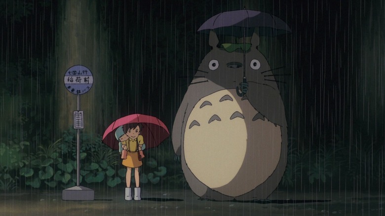 Satsuki and Mei waiting at a bus stop in the rain next to a giant furry Totoro in My Neighbor Totoro.