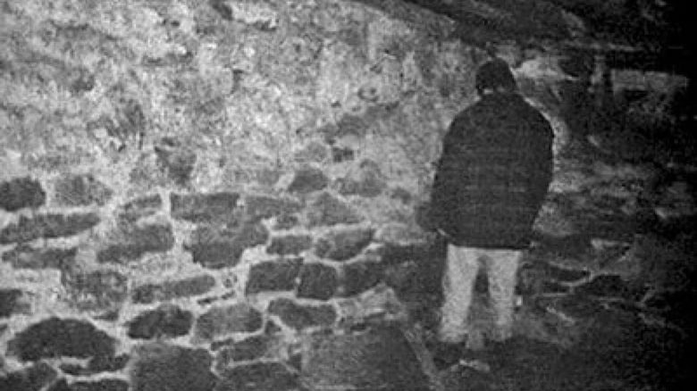 a man facing the corner in a room with stone walls