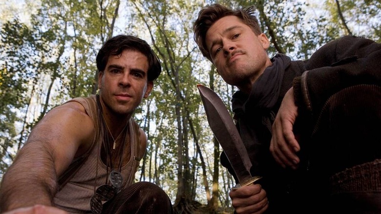 two men looking down at someone from above in the forest and the right one has a knife