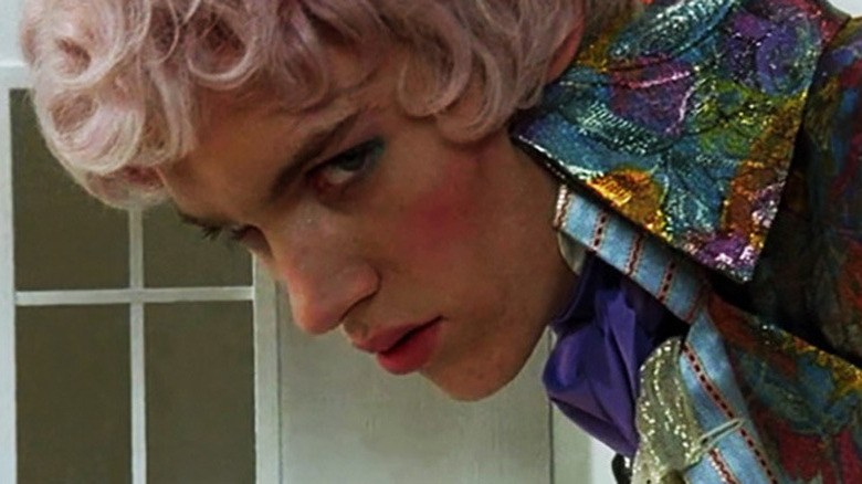 a man with cropped pink hair and a multicolored jacket looking down and toward the camera