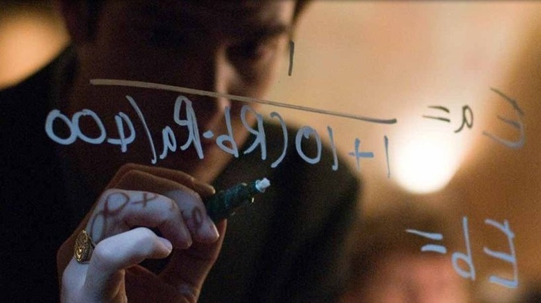 a man writing mathematic equations on a see-through board