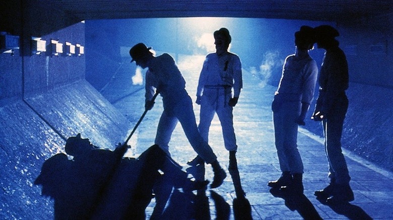 a man in a bowler hat pokes a man on the ground with a stick while three other men watch