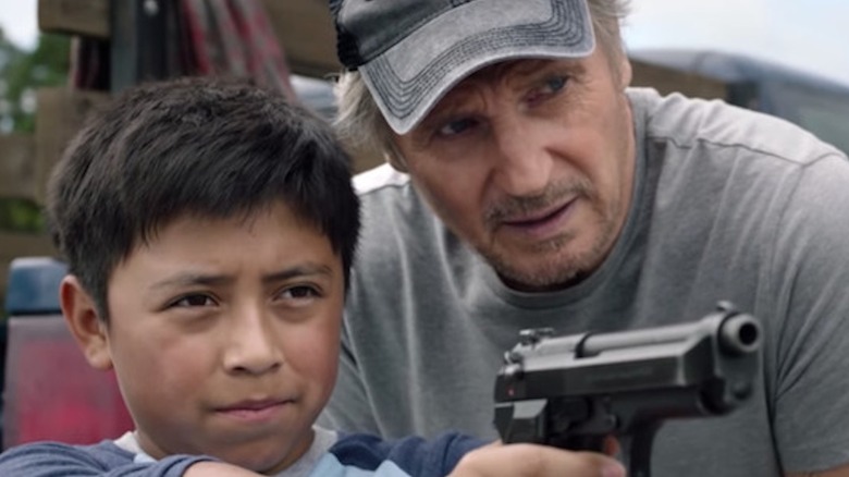 Liam Neeson as Jim Hanson tenderly teaches young Jacob Perez as Miguel to fire a handgun in The Marksman