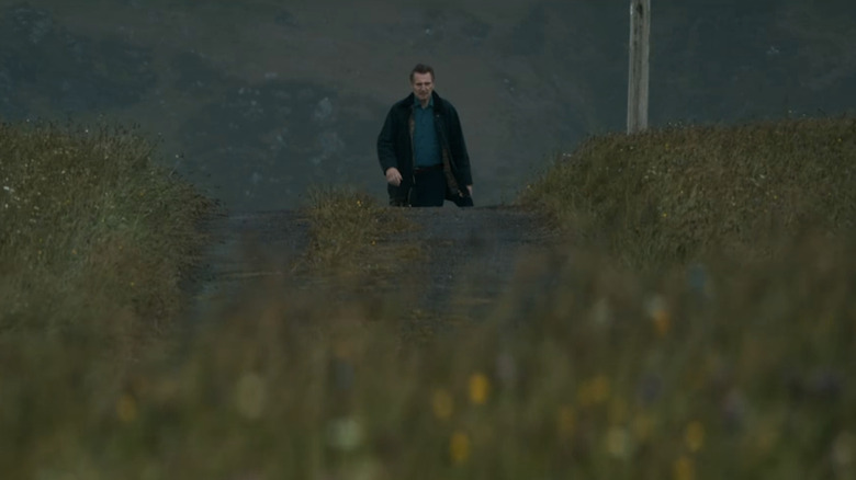 Liam Neeson's Finbar Murphy walks on a road through a field in In the Land of Saints and Sinners