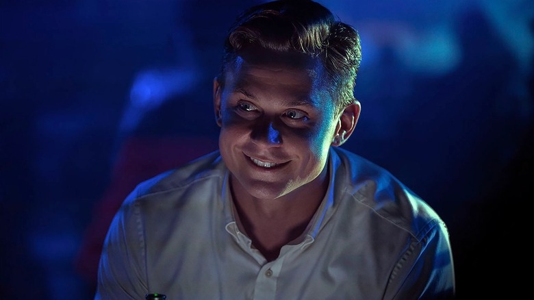 Billy Magnussen flashes a toothy grin as Logan Ash in No Time to Die