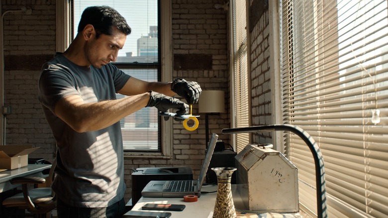Ash wearing gloves and cutting a roll of tape in an apartment in Relay