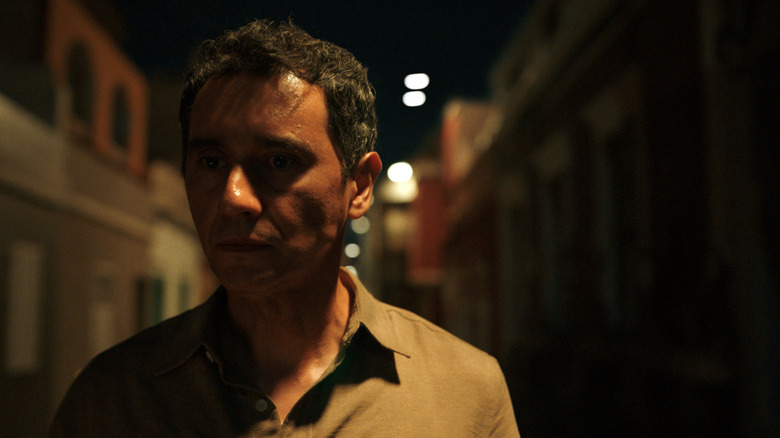 Carlos-Manuel Vesga as Manousos standing ominously in an empty street in Pluribus