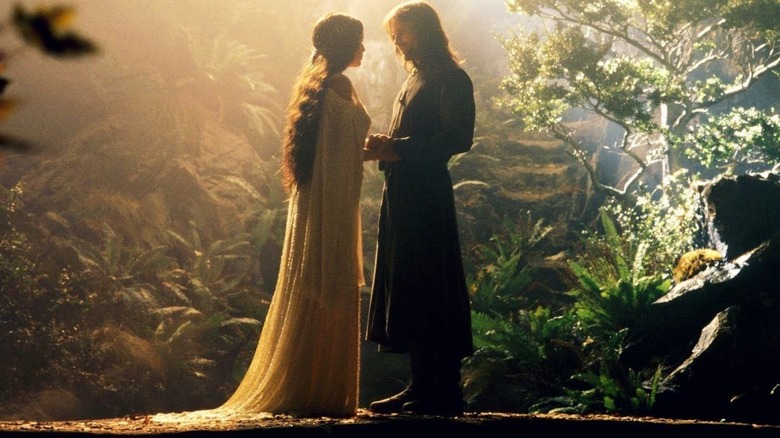 Arwen and Aragorn stand on a bridge in a garden holding hands