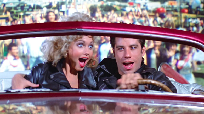 John Travolta's Danny Zuko sits beside Olivia Newton-John's Sandy Olsson in a car as they take off from a field in Grease