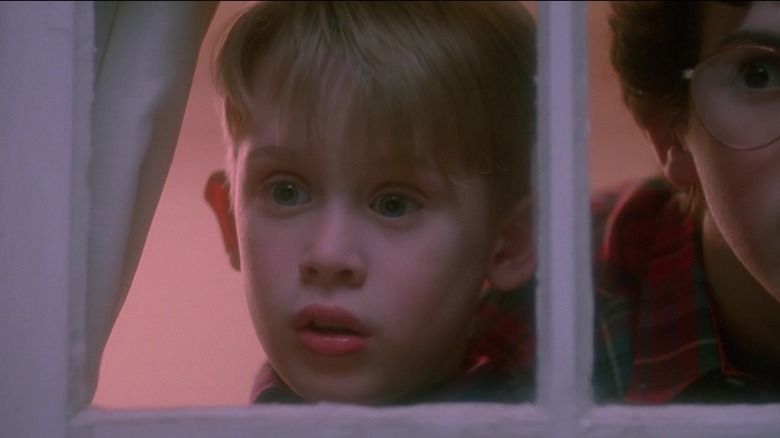 Kevin McCallister van Macaulay Culkin ziet er bang uit als hij uit een raam tuurt in Home Alone