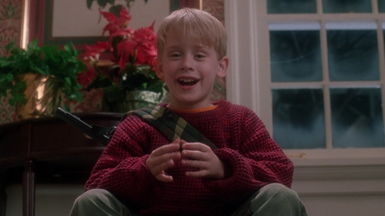 Kevin McCallister van Macaulay Culkin glimlacht terwijl hij boven aan zijn trap hurkt in Home Alone