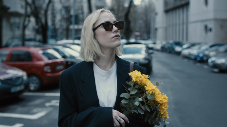 Maika Monroe's Julia carries flowers while walking on a Bucharest street in Watcher