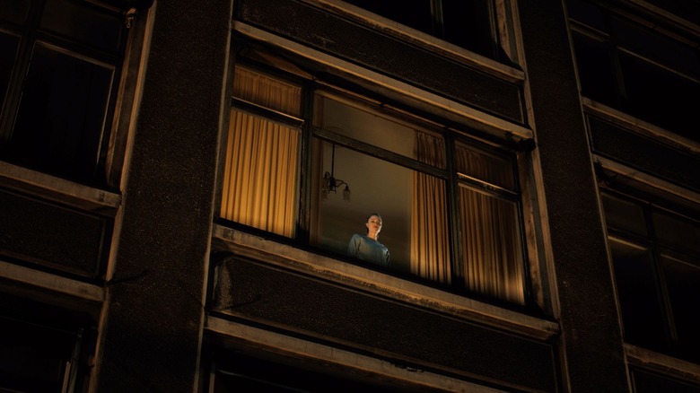 Julia stares out a window from behind a curtain in Watcher