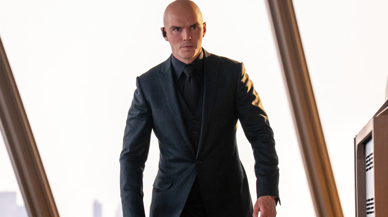 Nicholas Hoult as Lex Luthor wearing a suit and earpiece while standing menacingly in his office by a window in Superman