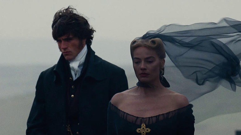 वुथरिंग हाइट्स (२०२६) मध्ये काळ्या पोशाखात कॅथरीनच्या भूमिकेत मार्गोट रॉबीच्या शेजारी चालत असलेल्या हिथक्लिफच्या भूमिकेत जेकब एलॉर्डी