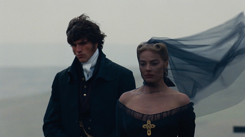 Healthcliff and Catherine walking along a cliffside wearing black in Wuthering Heights