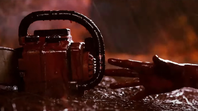 A hand reaching for a chainsaw while it rains blood in Evil Dead