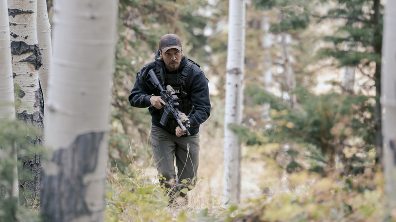 Luke Grimes' Kayce Dutton runs through a forest with a gun in Marshals