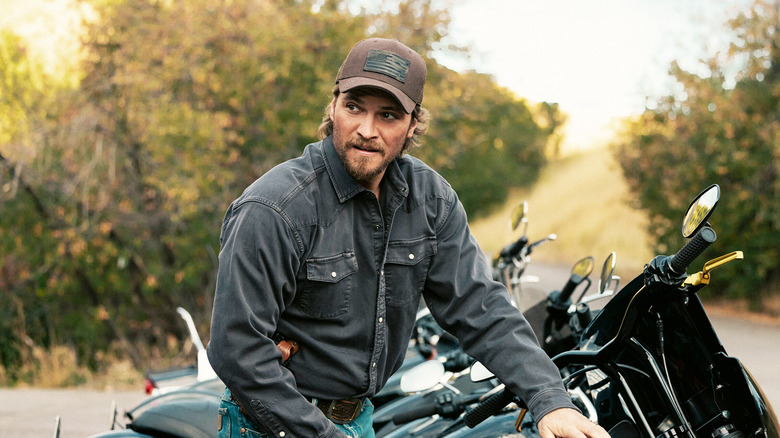 Luke Grimes' Kayce Dutton looks off to his right as he stands by a line of motorcycles in Marshals