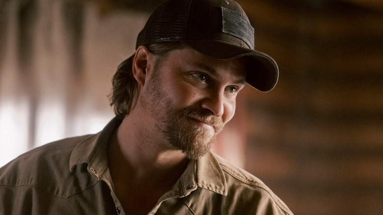 Luke Grimes' Kayce Dutton smiles as he stands in his cabin in Marshals