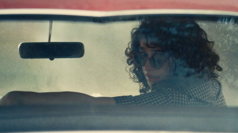 Rachel sits in a car and looks out the back window in Marty Supreme