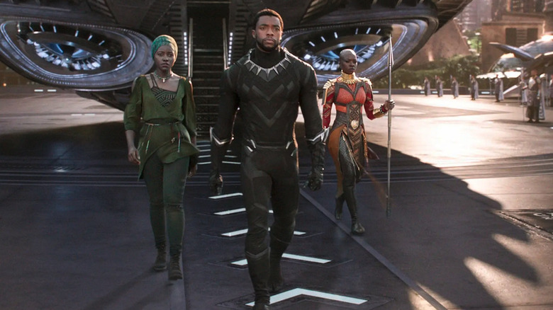 T'Challa (Chadwick Boseman) walks with Nakia (Lupita Nyong'o) and Okoye (Danai Gurira) from a ship in Black Panther