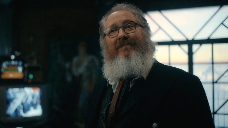 James Spader as Ultron in his human avatar standing in a loft with several television screens in the background in VisionQuest