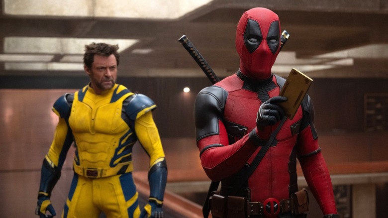 Ryan Reynolds as Deadpool speeaking to the TVA with Hugh Jackamn as Wolverine hanging out behind him in Deadpool & Wolverine