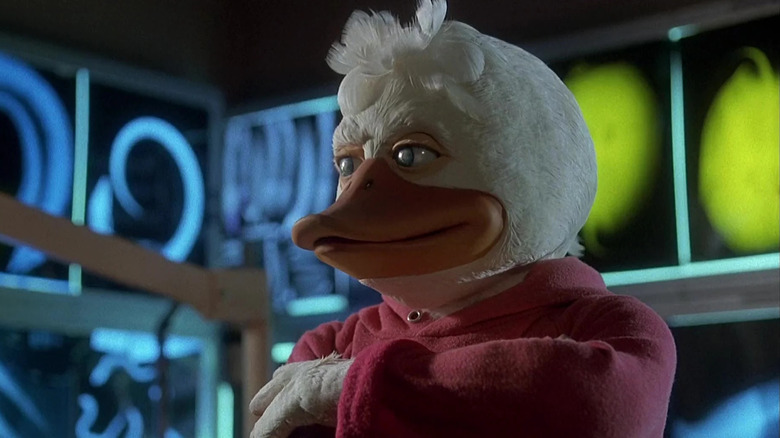 Howard o pato em um capuz vermelho, taciturno em pé em frente a algumas luzes de neon. De Howard the Duck.