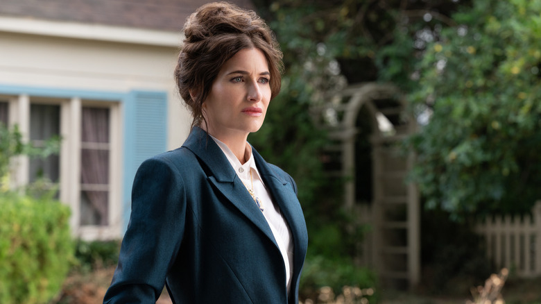 Kathryn Hahn sebagai Agatha Harkness dengan tangannya di sakunya berdiri di luar rumah di Agatha selama ini