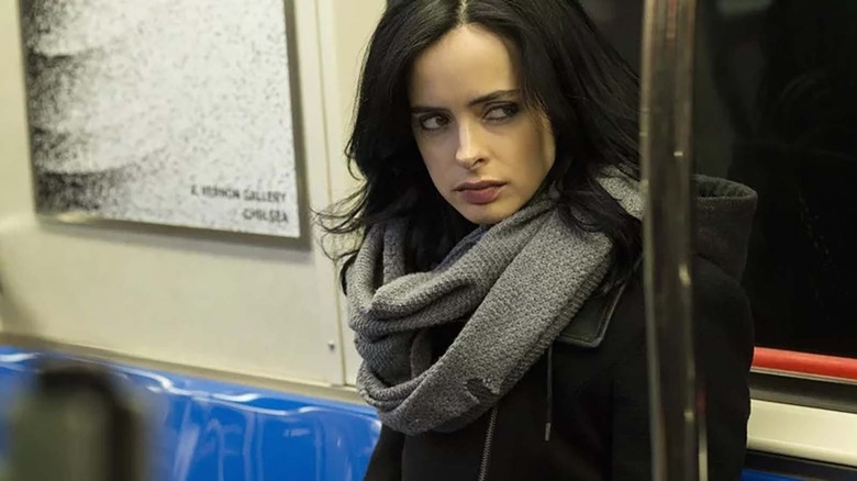 woman sitting on the train looking to her left in a black jacket and grey scarf