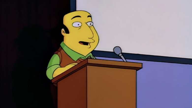 జే షెర్మాన్ ది సింప్సన్స్‌లోని పోడియం వద్ద నిలబడి ఉన్నాడు
