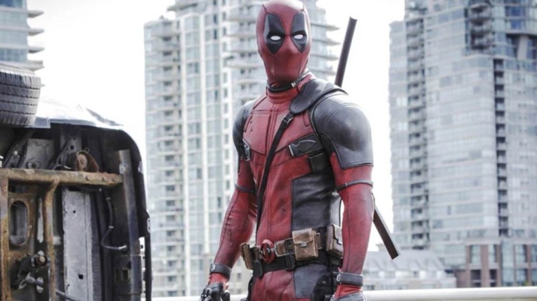 Deadpool stood in front of towers and a turned over car