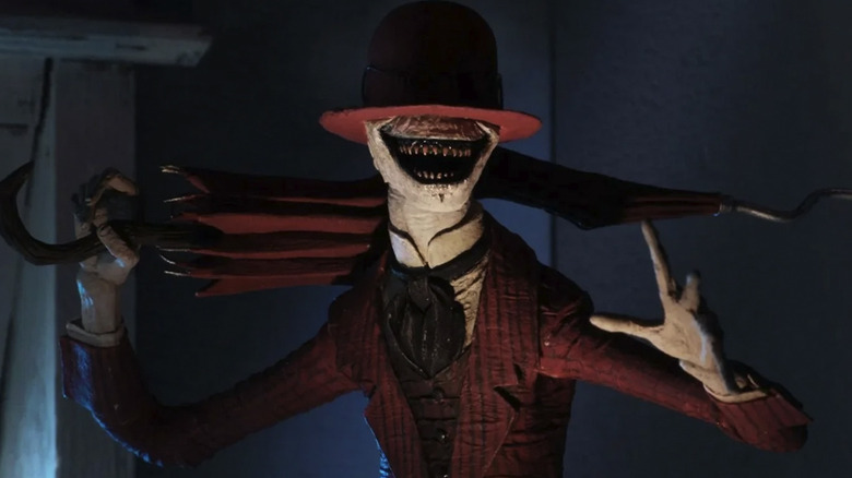 The Crooked Man holds a twisted umbrella and smiles in The Conjuring 2