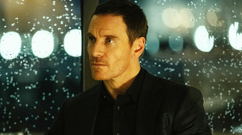 Michael Fassbender's Brandon Colby sits against a window with rain drops in The Agency