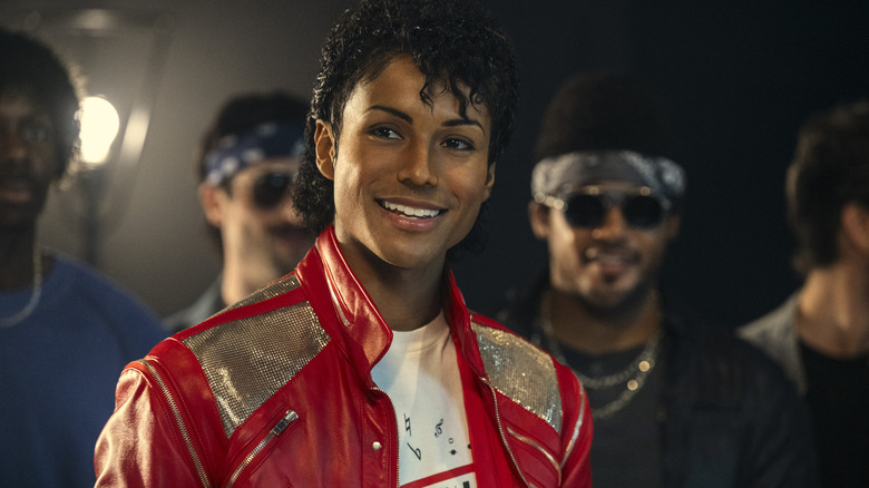Jaafar Jackson as Michael Jackson wearing a red jacket and smiling on stage in Michael