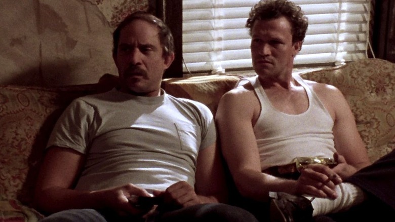 Tom Towles' Otis sitting on the sofa with Michael Rooker's Henry in Henry: Portrait of a Serial Killer