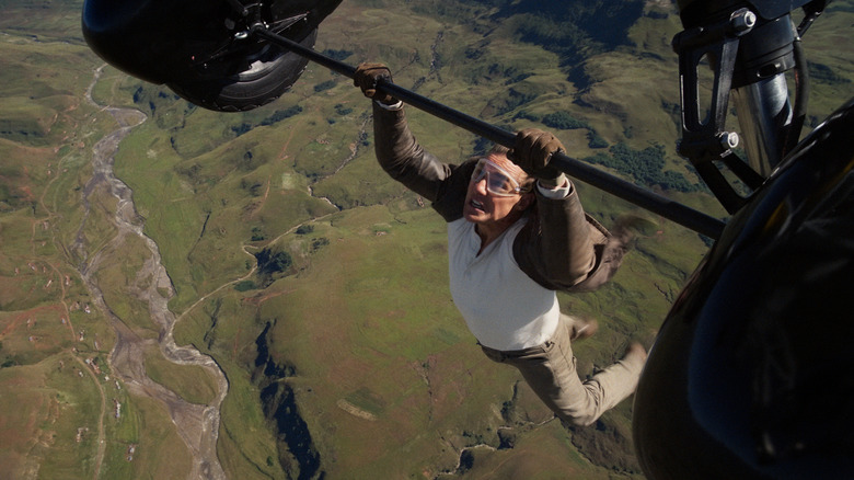 Tom Cruise as Ethan Hunt hanging from the bottom of a biplane midair in Mission: Impossible - The Final Reckoning