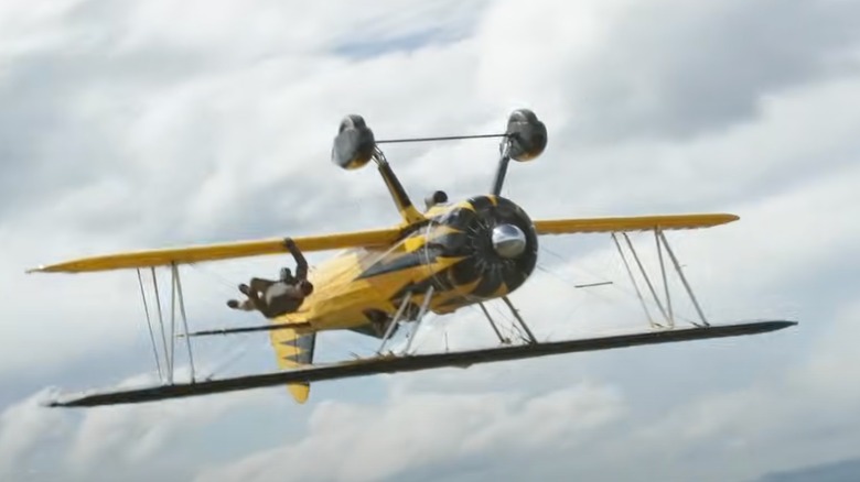 Ethan Hunt (TOM CRUISE) hanging on the side of a two -dimensional panels wing as it flies upside down through a cloudy sky