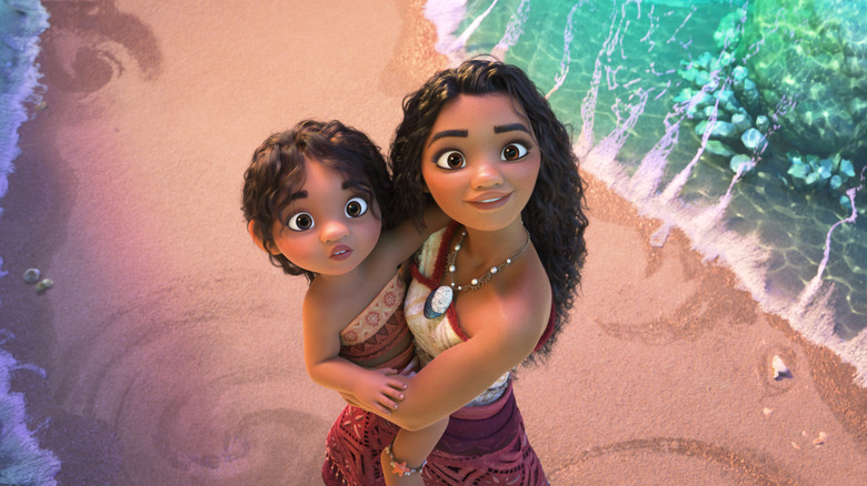 Auli'i Cravalho as Moana holds Khaleesi Lambert-Tsuda as Simea and looks up on the beach in Moana 2